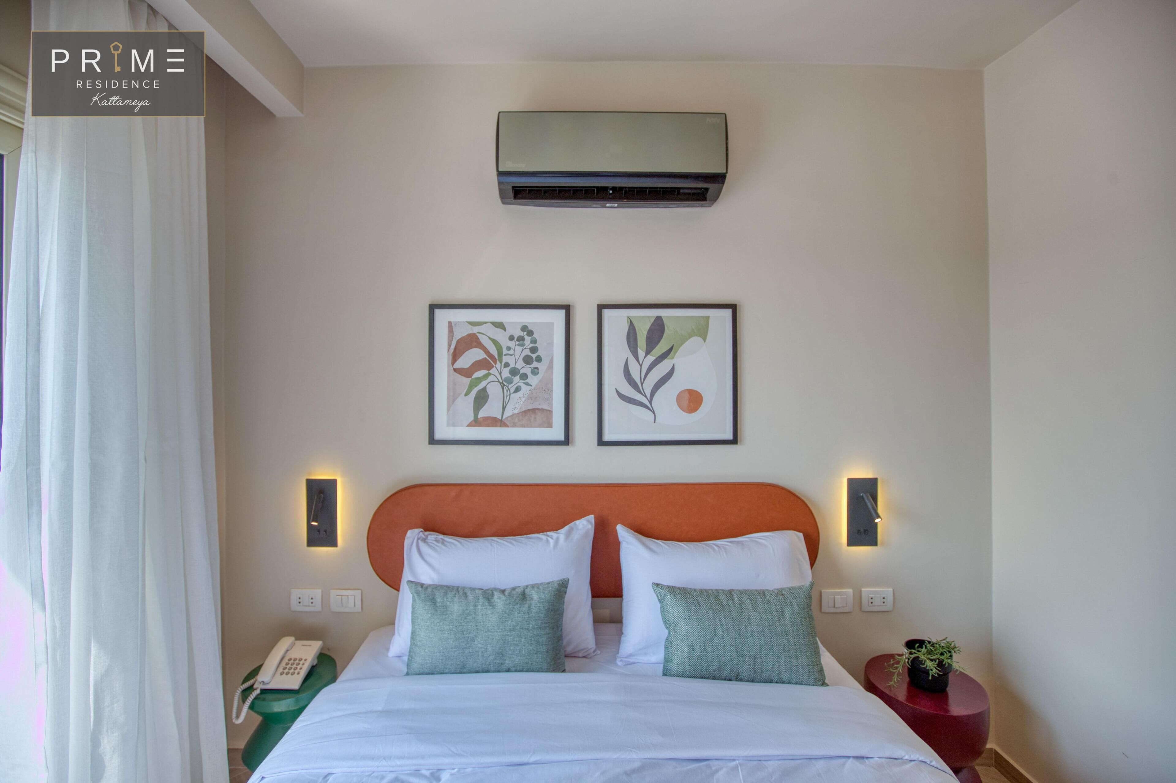 Ein Hotelzimmer mit einem Bett, zwei Wandleuchten, einer Klimaanlage und zwei gerahmten Kunstwerken.