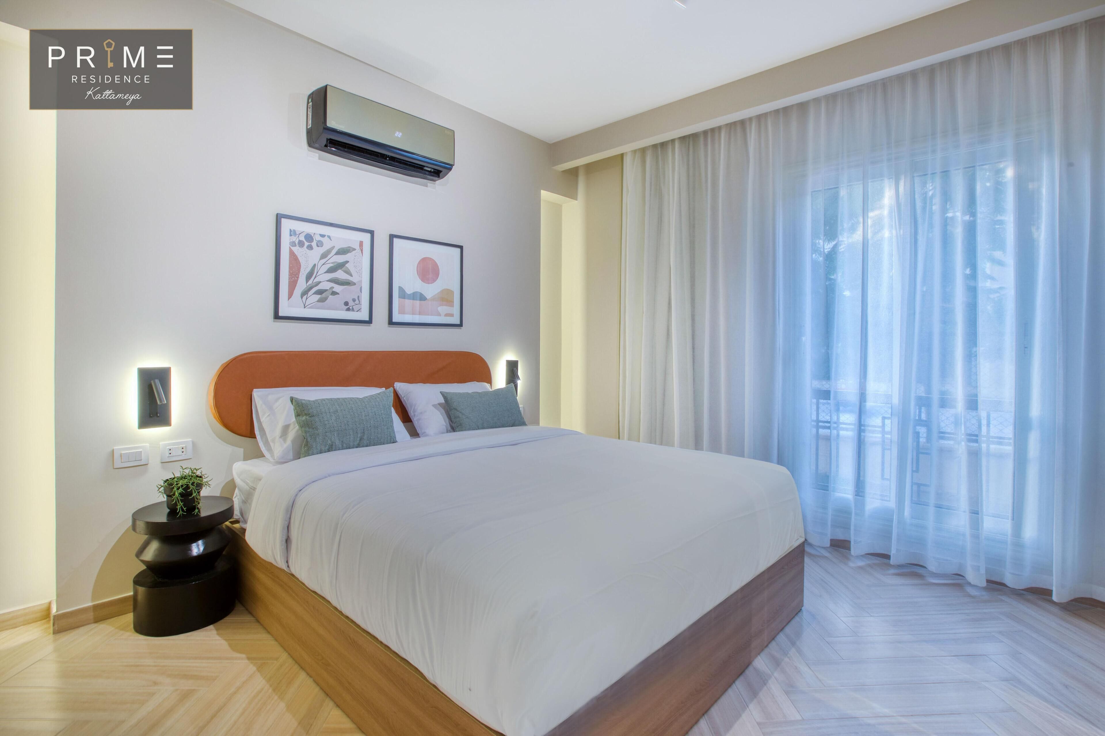 A modern hotel room with a large bed, a wall-mounted air conditioner, and two framed artworks.