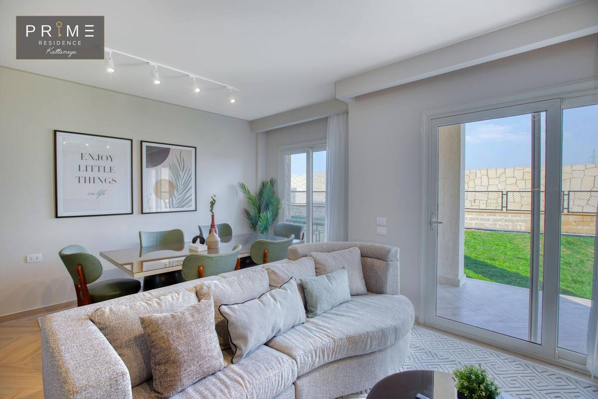 A modern living room with a sofa, dining table, chairs, and a large sliding glass door leading to a patio.