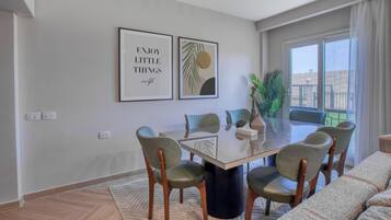 A dining area with a glass table, six chairs, two framed artworks, and a potted plant.