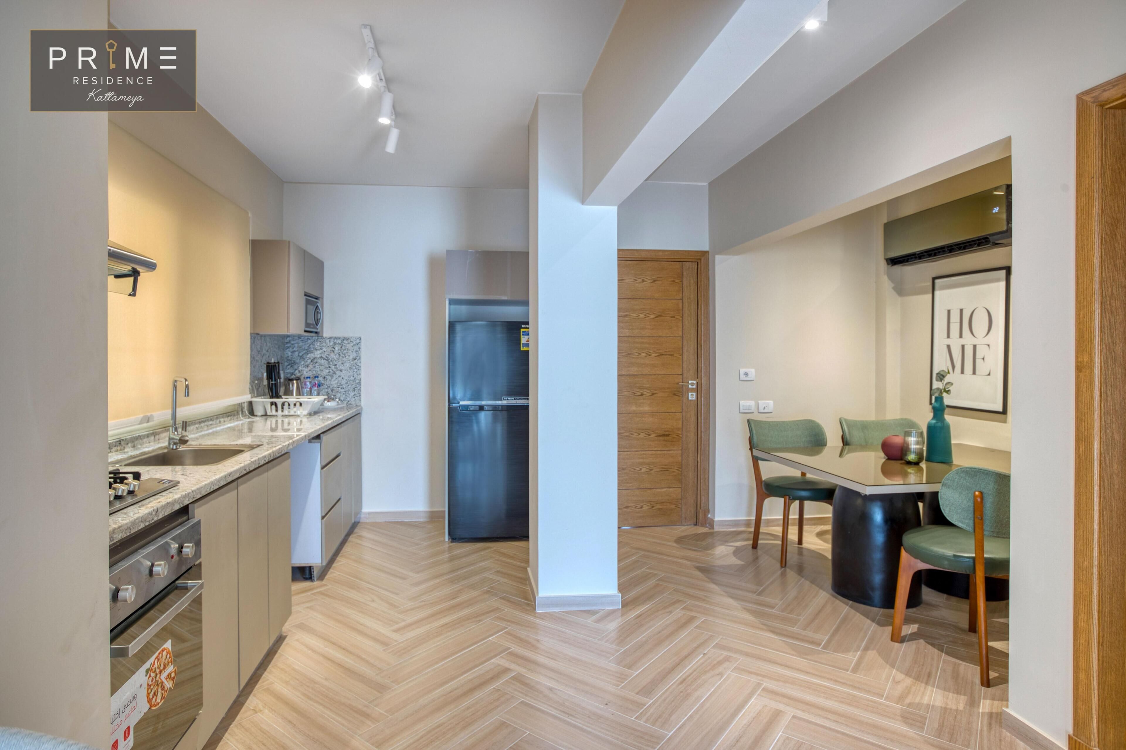 A modern kitchen with a built-in oven, a stainless steel refrigerator, and a dining area with a table and chairs.