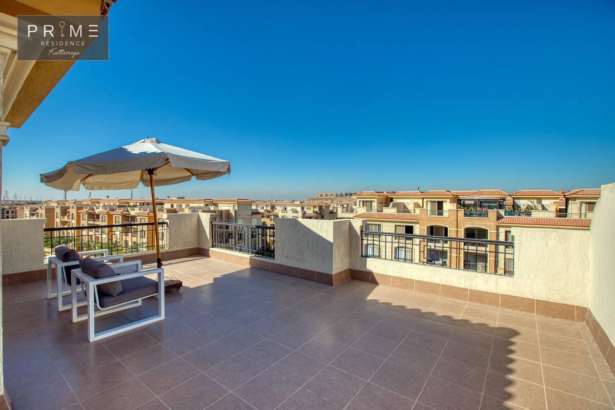 A rooftop terrace with a clear view of the cityscape, featuring a seating area with a table and chairs, and a large umbrella.