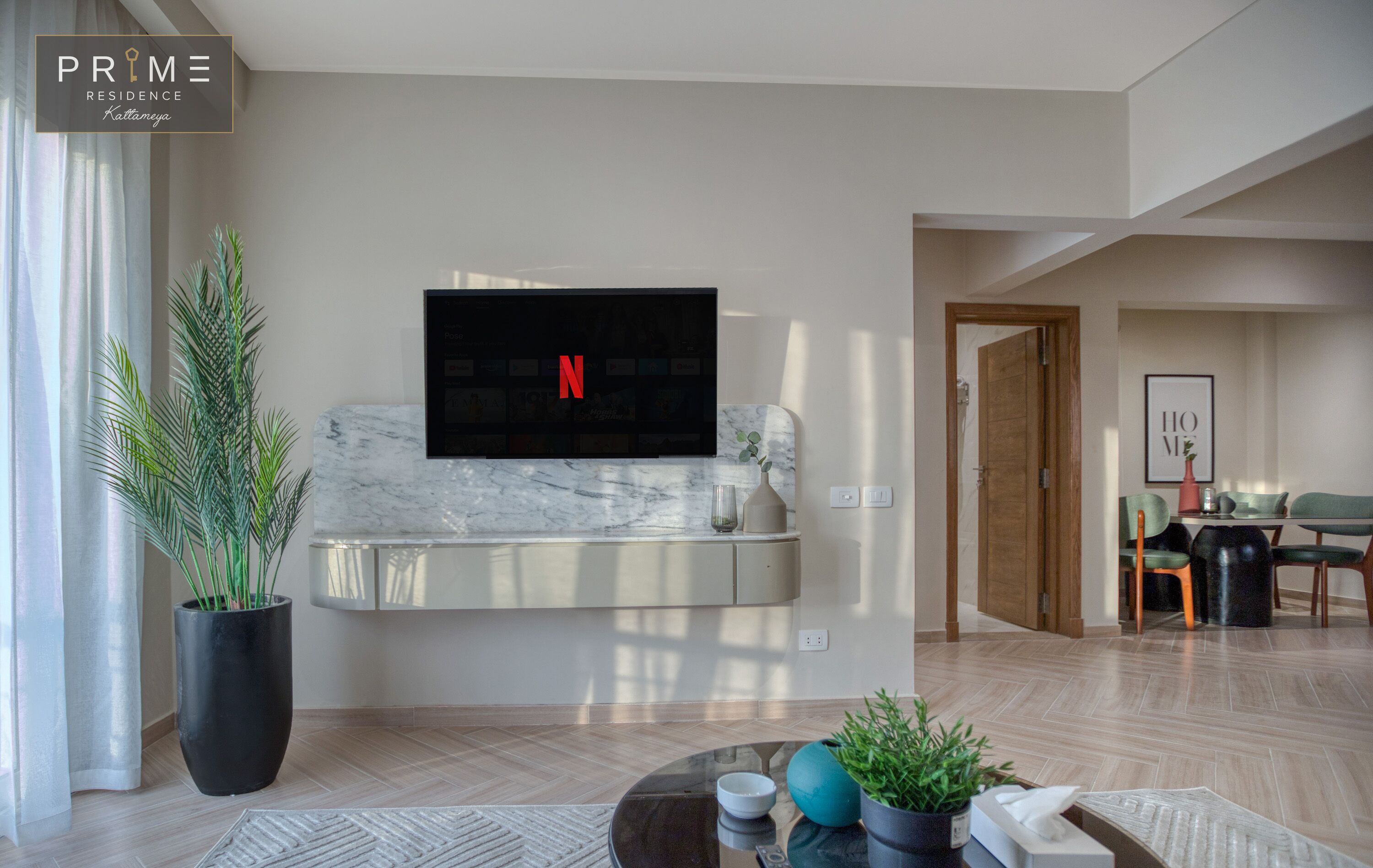 Un salon moderne avec un téléviseur à écran plat fixé au mur, un comptoir en marbre, une plante en pot et un coin repas comprenant une table et des chaises.