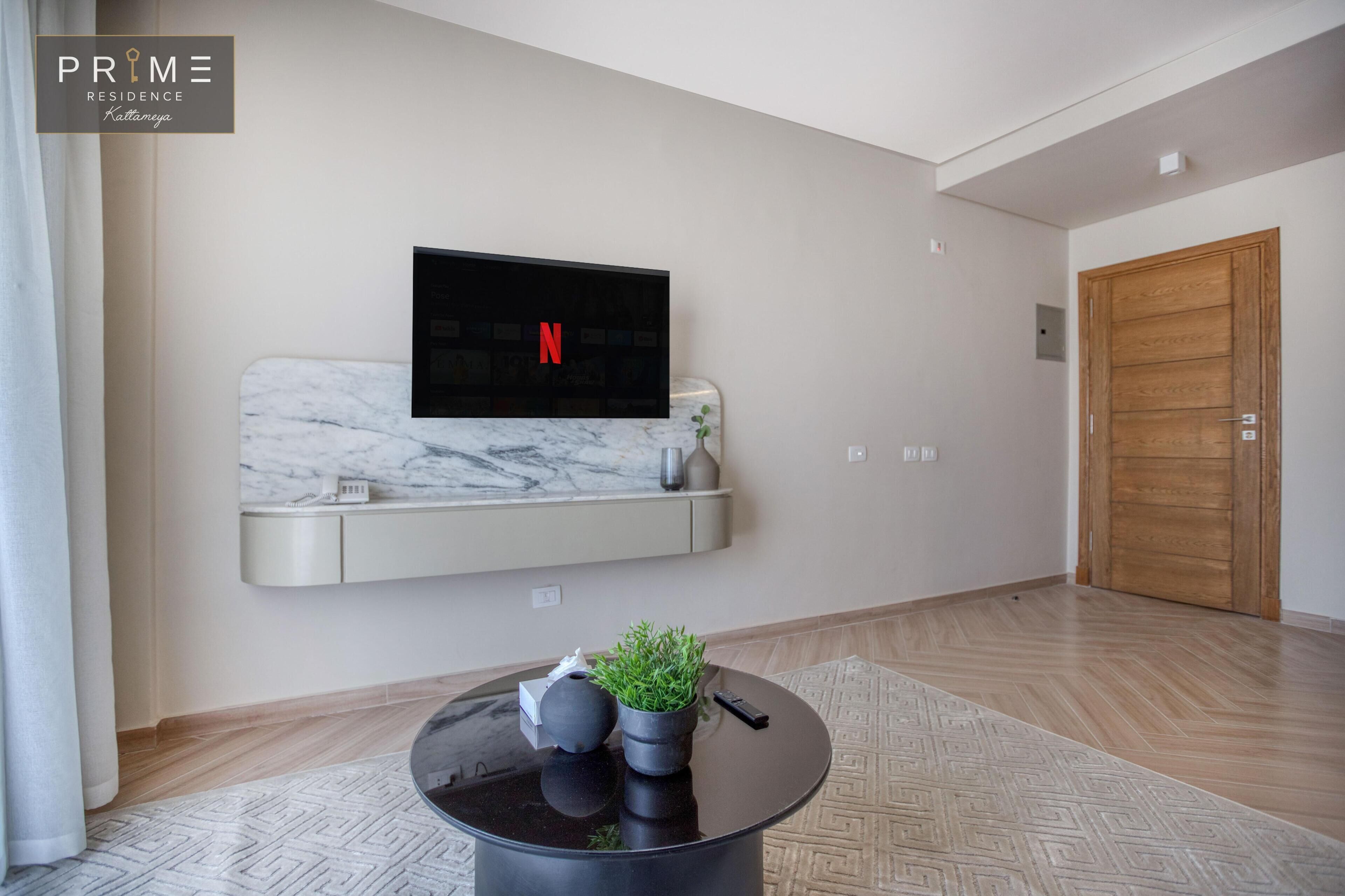 Een moderne woonkamer met een wandgemonteerde televisie, een marmeren plank, potplanten en een ronde salontafel.