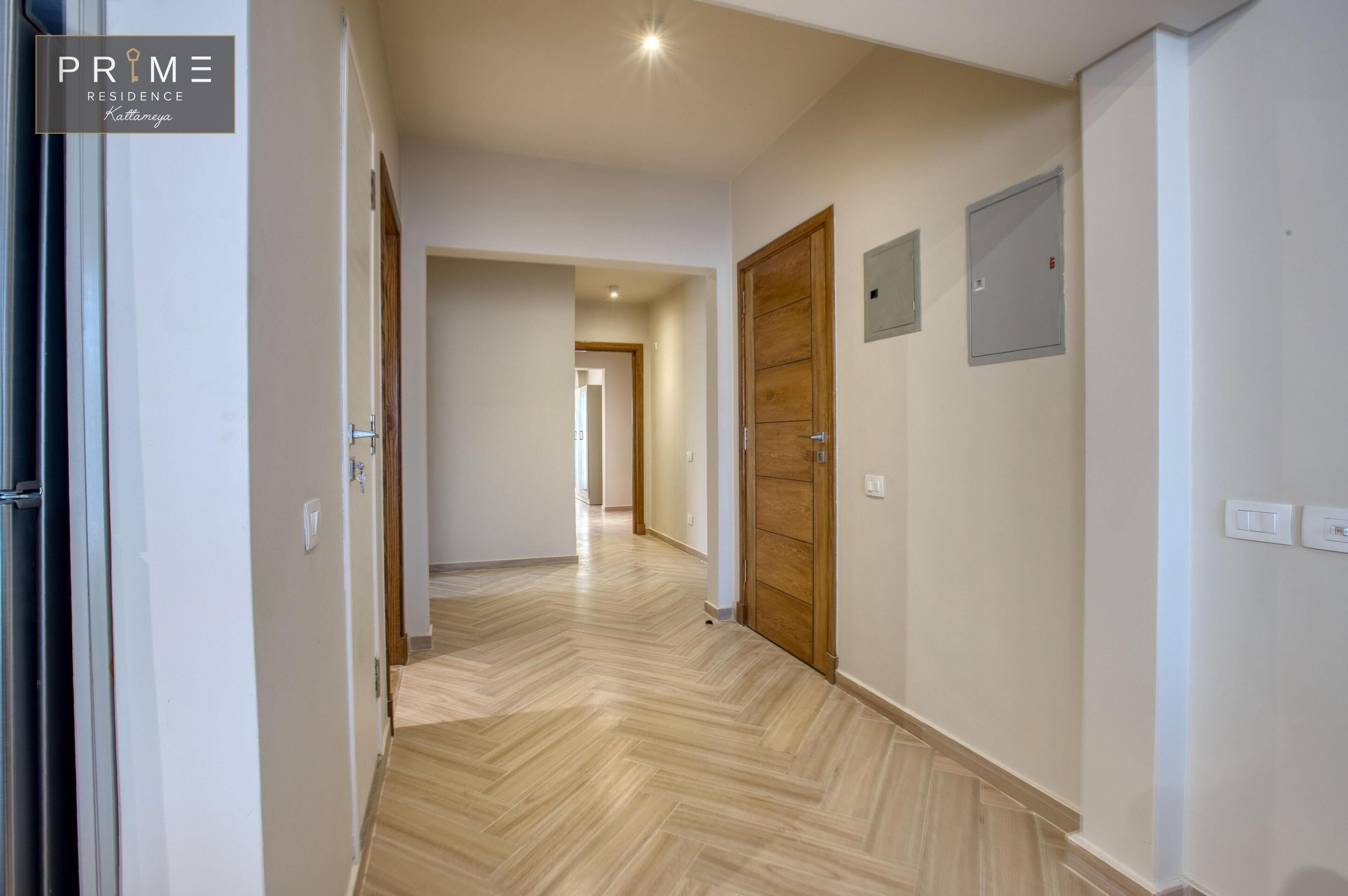 Un couloir doté d’un plancher en bois, de murs blancs et d’une porte en bois au fond.