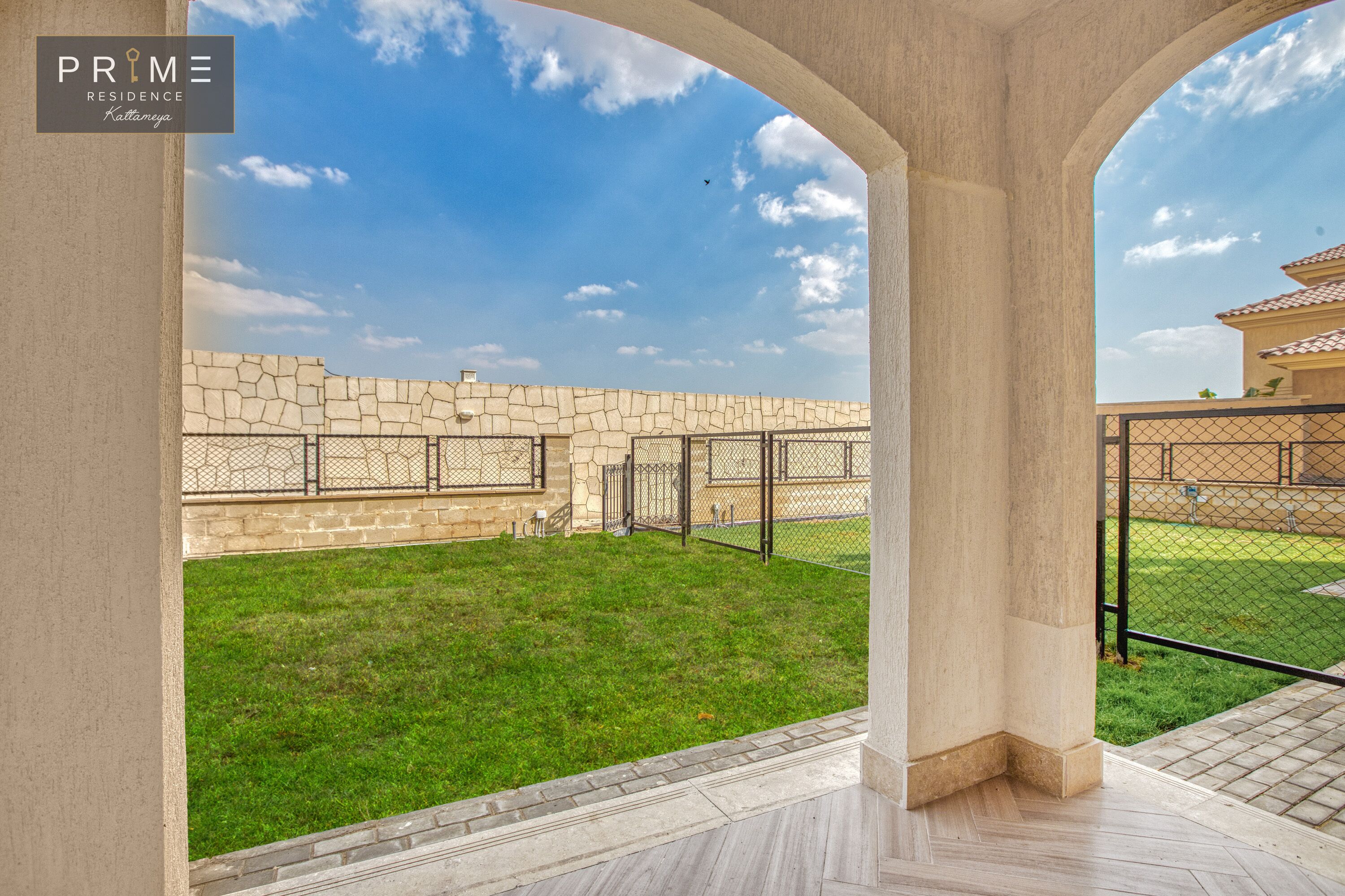 A courtyard with a stone wall, a grassy area, and a metal fence.