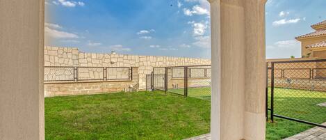 A courtyard with a stone wall, a grassy area, and a metal fence.