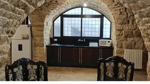A stone-walled kitchen with a window, a refrigerator, and a microwave.