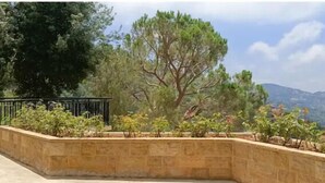 A landscaped garden with a large tree, stone retaining wall, and a metal fence.