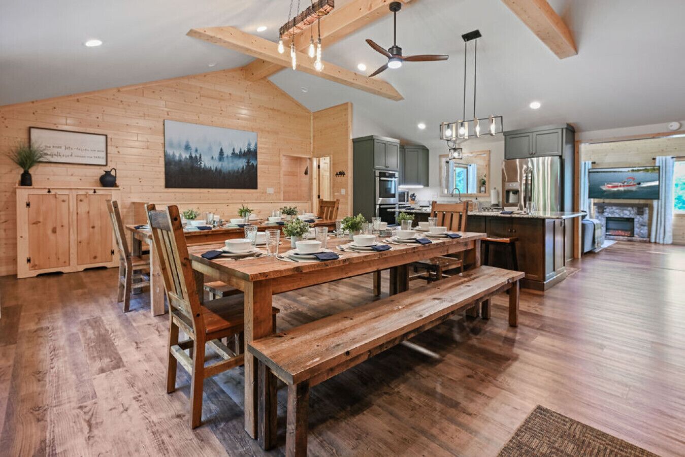 A spacious kitchen with wooden cabinets, a dining area with a large wooden table and benches, and a ceiling fan.