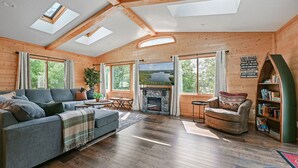 A cozy log cabin interior with a fireplace, a sofa, a chair, and a bookshelf. - Elevated 6BR Lodge | On Trail | Speakeasy/Game Room (Eagle River)