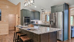 A modern kitchen with a central island, stainless steel appliances, and wooden cabinetry. - Elevated 6BR Lodge | On Trail | Speakeasy/Game Room (Eagle River)