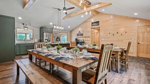 A dining area with a wooden table set for four, a ceiling fan, and a 'Welcome' sign on the wall. - Elevated 6BR Lodge | On Trail | Speakeasy/Game Room (Eagle River)