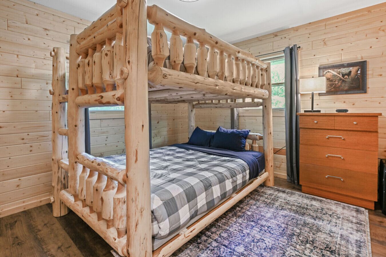 Un dormitorio de cabaña de madera con una cama superpuesta, un aparador y una alfombra.