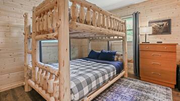 Un dormitorio de cabaña de madera con una cama superpuesta, un aparador y una alfombra.