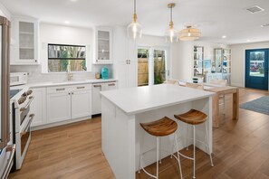 Una cocina moderna con armarios blancos, una isla central con taburetes e iluminación colgante.