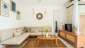 Un soggiorno moderno con un divano componibile, un tavolino in legno, un televisore su un mobile in legno e una pianta di cactus.