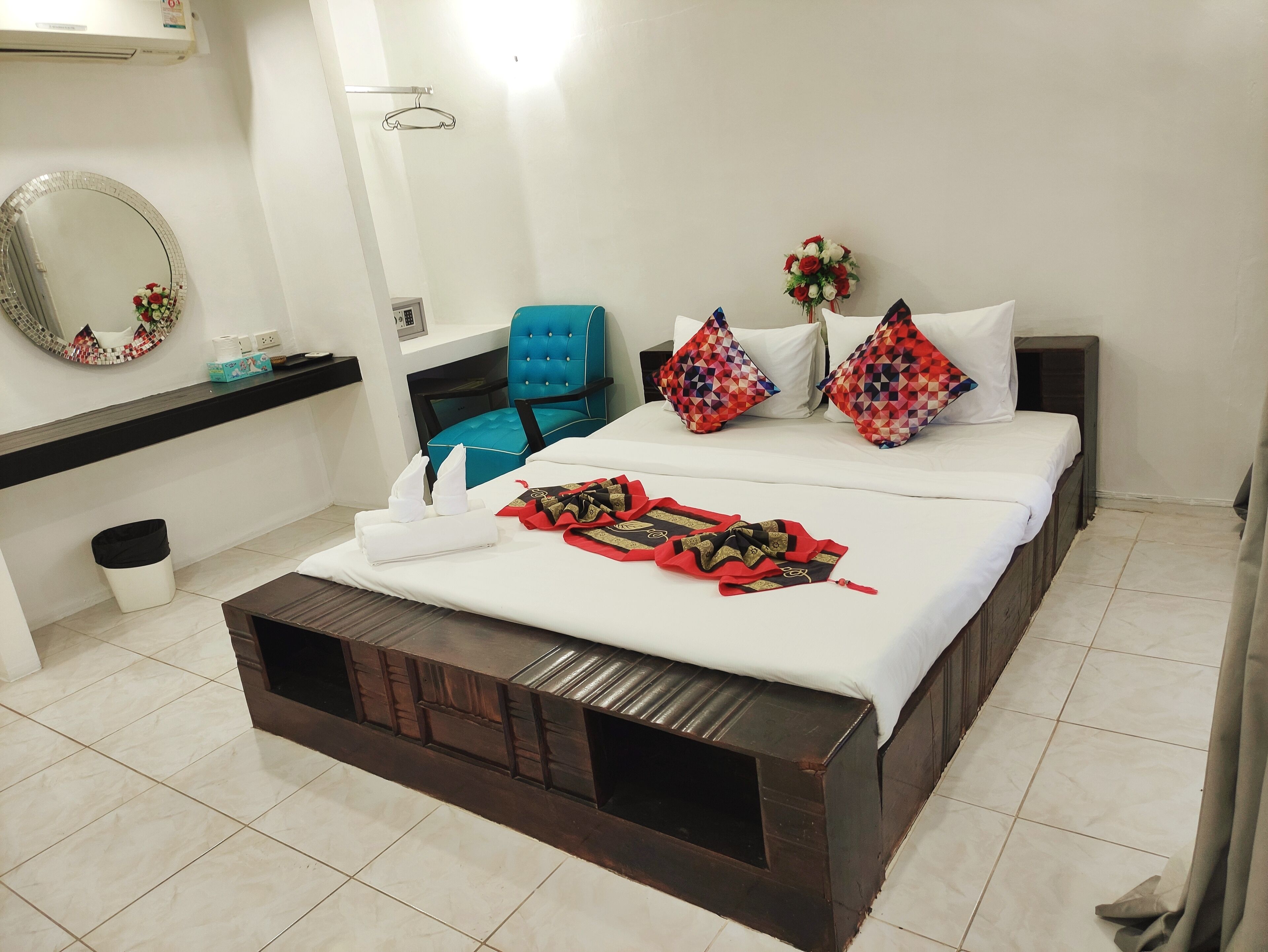 Een hotelkamer met een groot bed, een blauwe stoel, een kleine prullenbak en een spiegel aan de muur.