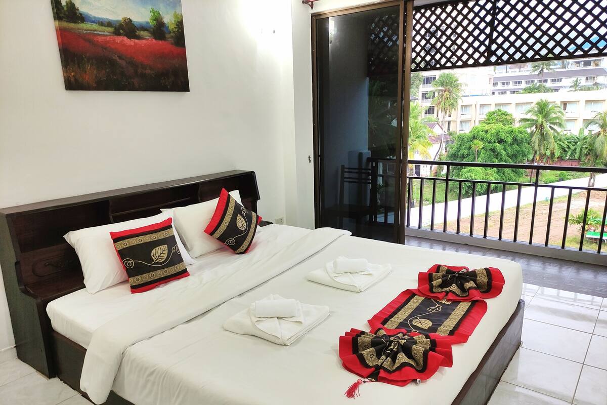 A hotel room with a neatly made bed, a balcony with a view of the city, and a painting on the wall.