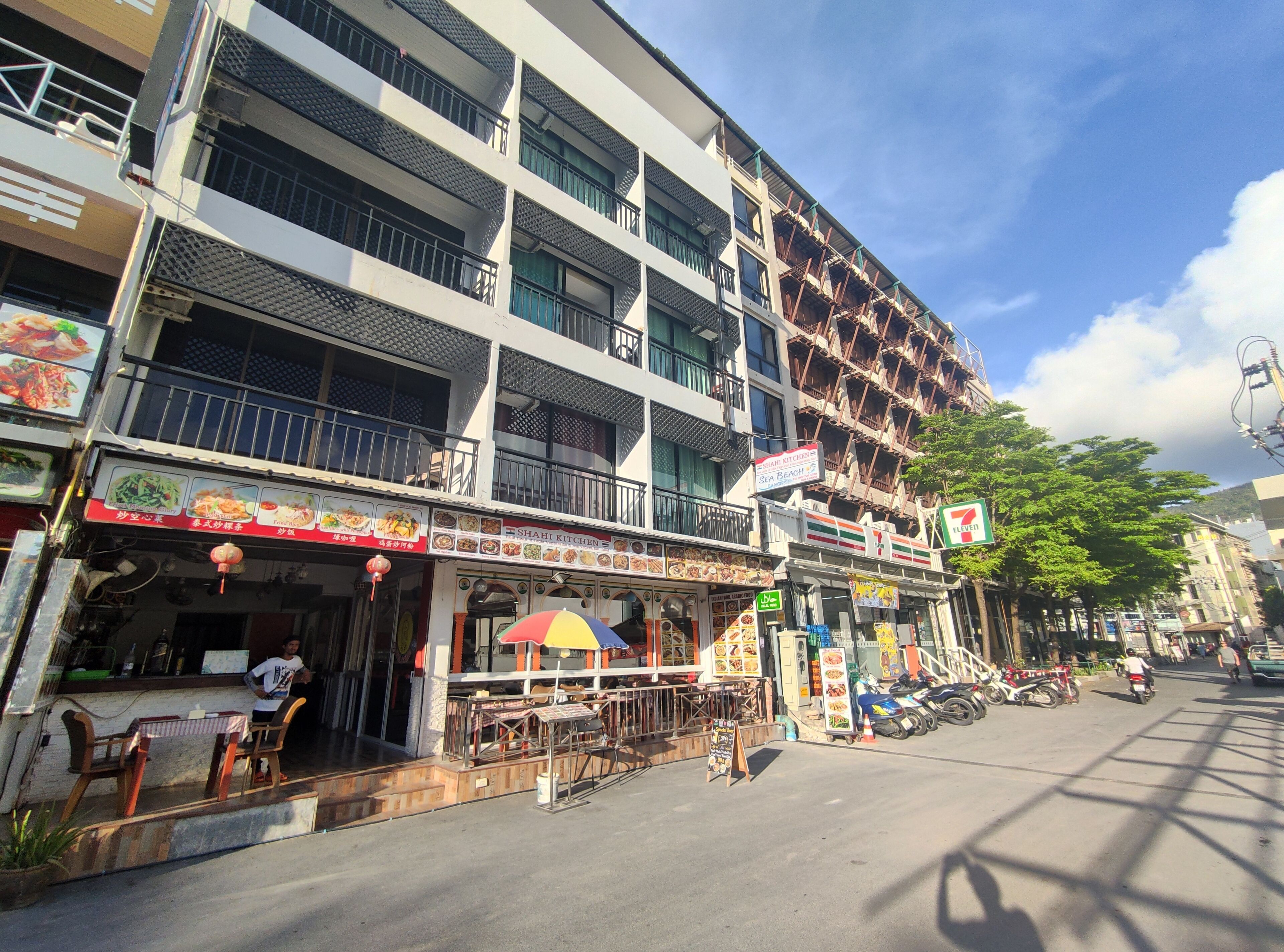 Un edificio de varios pisos con un restaurante en la planta baja, una tienda de conveniencia 7-Eleven y un cartel de Shahi Kitchen.