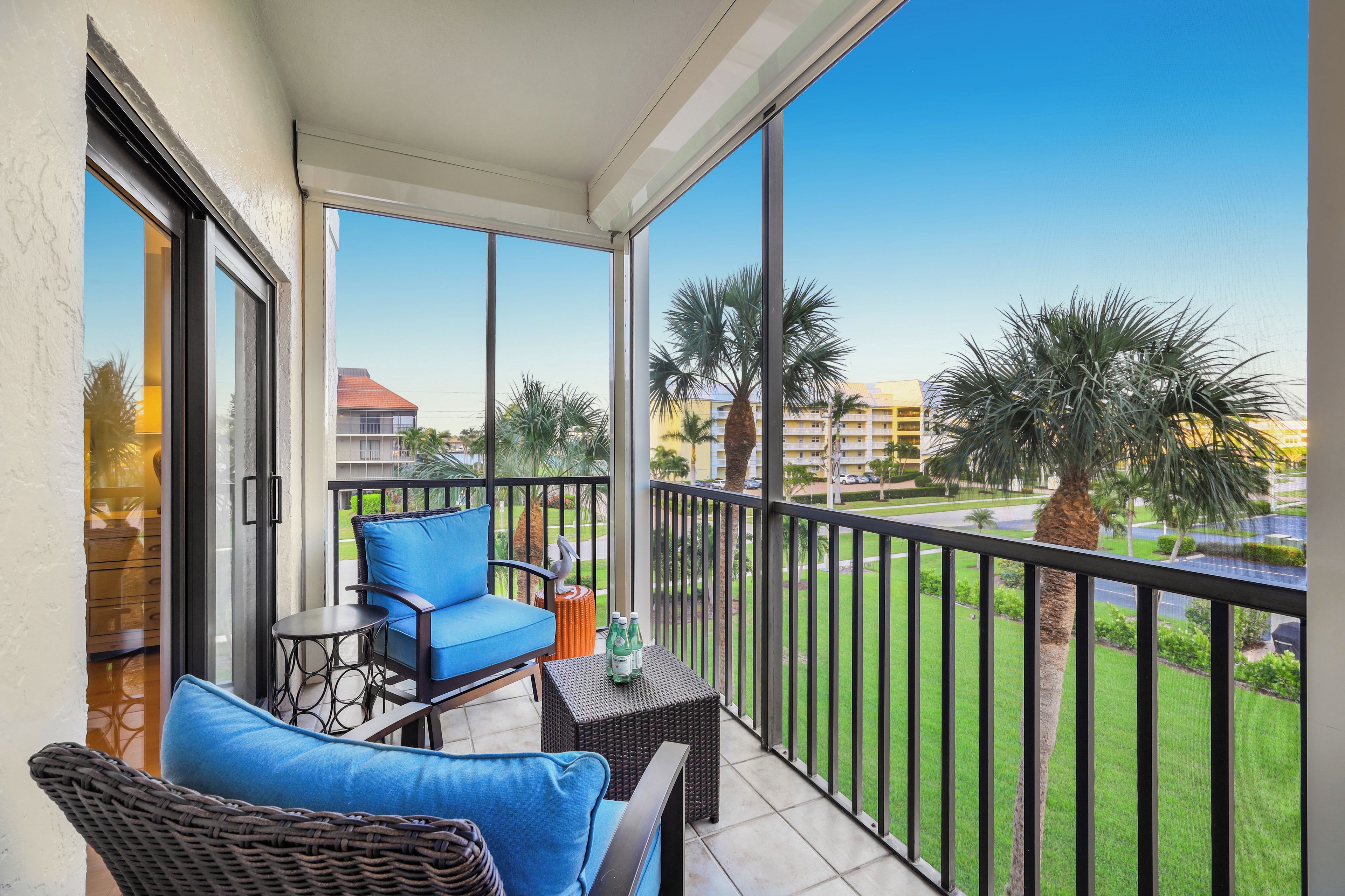 A balcony with a blue sofa, wicker chairs, and a small table with bottles.