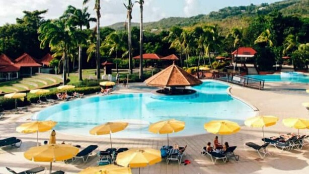 A resort pool area with sun loungers and umbrellas, surrounded by palm trees and a hilly landscape. - Studio Tropical Avec vue sur le Rocher du Diamant (Sainte-Luce)