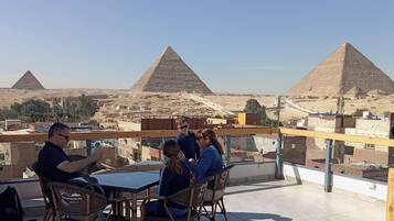 Une terrasse sur le toit offrant une vue sur les pyramides, avec une table et des chaises, et un ciel dégagé.