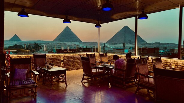 A restaurant with a view of the pyramids, featuring outdoor seating and blue pendant lighting. - Nun Pyramids INN (Giza)