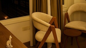 A room with a view of a pyramid at night, two chairs, a wooden table, and a small statue. - Nun Pyramids INN (Giza)