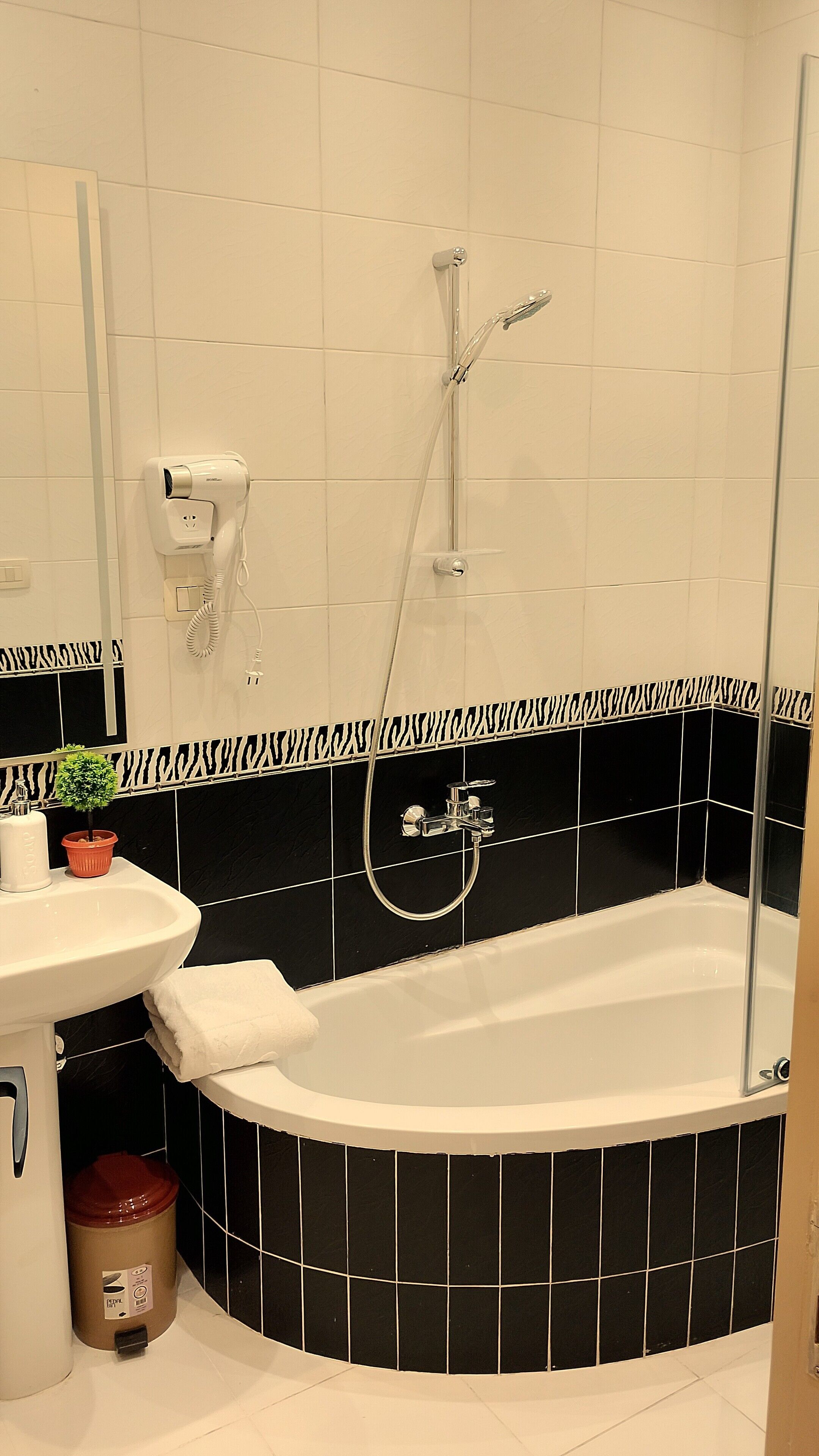 A bathroom with a bathtub, a sink, a mirror, and a hairdryer mounted on the wall.