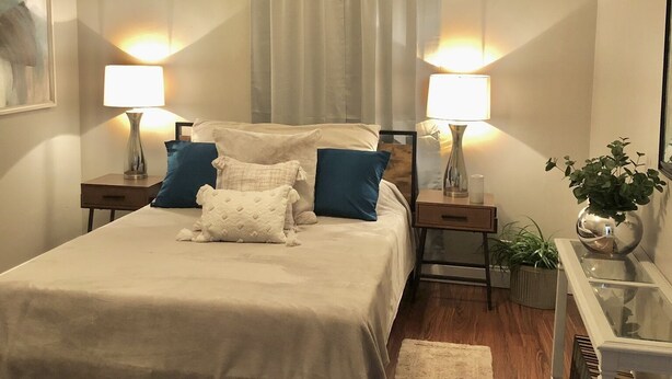 A bedroom with a bed, two bedside tables with lamps, a nightstand, a potted plant, and a painting on the wall. - Historic Home Steps from Florida Southern, Lake Morton and Lake Hollingsworth (Lakeland)