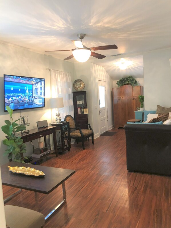 A living room with a television, wooden furniture, a ceiling fan, and a dining area.