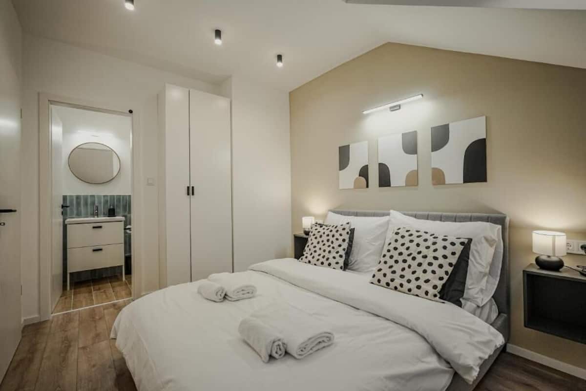 Ein modernes Schlafzimmer mit einem ordentlich bezogenen Bett, einem Nachttisch mit Lampe und einem an der Wand hängenden Kunstwerk.