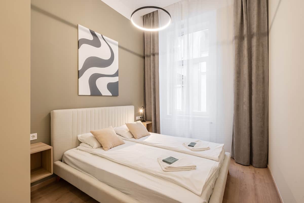 Ein modernes Schlafzimmer mit einem großen Bett, Nachttischen, einem Wandbild und einem Fenster mit Vorhängen.