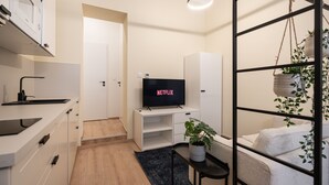 Un salón moderno con un televisor de pantalla plana, una zona de cocina con microondas y una sala de estar con sofá y planta colgante.