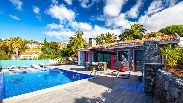Ein Swimmingpool mit Liegestühlen, einer Steinmauer und einer Terrasse mit Tisch und Stühlen.