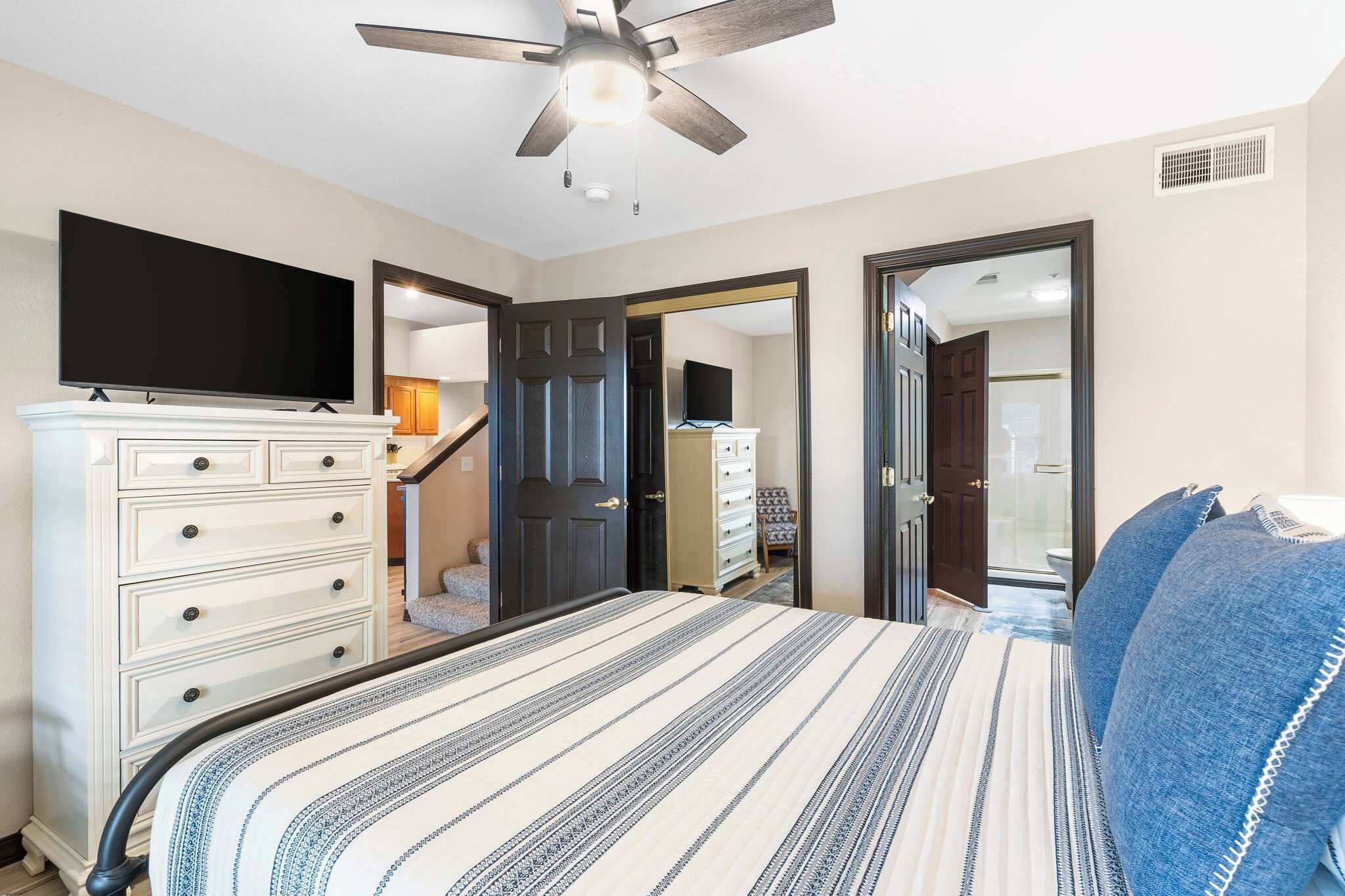 A bedroom with a bed, a dresser, a television, and a ceiling fan.