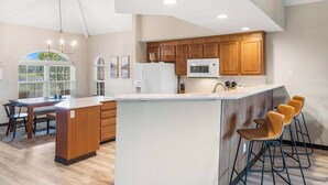 A modern kitchen with wooden cabinets, a white refrigerator, a microwave, and a bar area with stools.