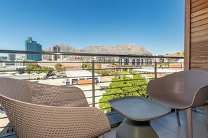 Un balcone con due sedie e un tavolino, affaccia su una città con edifici e una montagna.