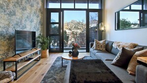 A modern living room with a large TV, a sofa, a coffee table, and a view of the outdoors through large windows. - Docklands Deluxe Apartments by ITC Hospitality (Cape Town)