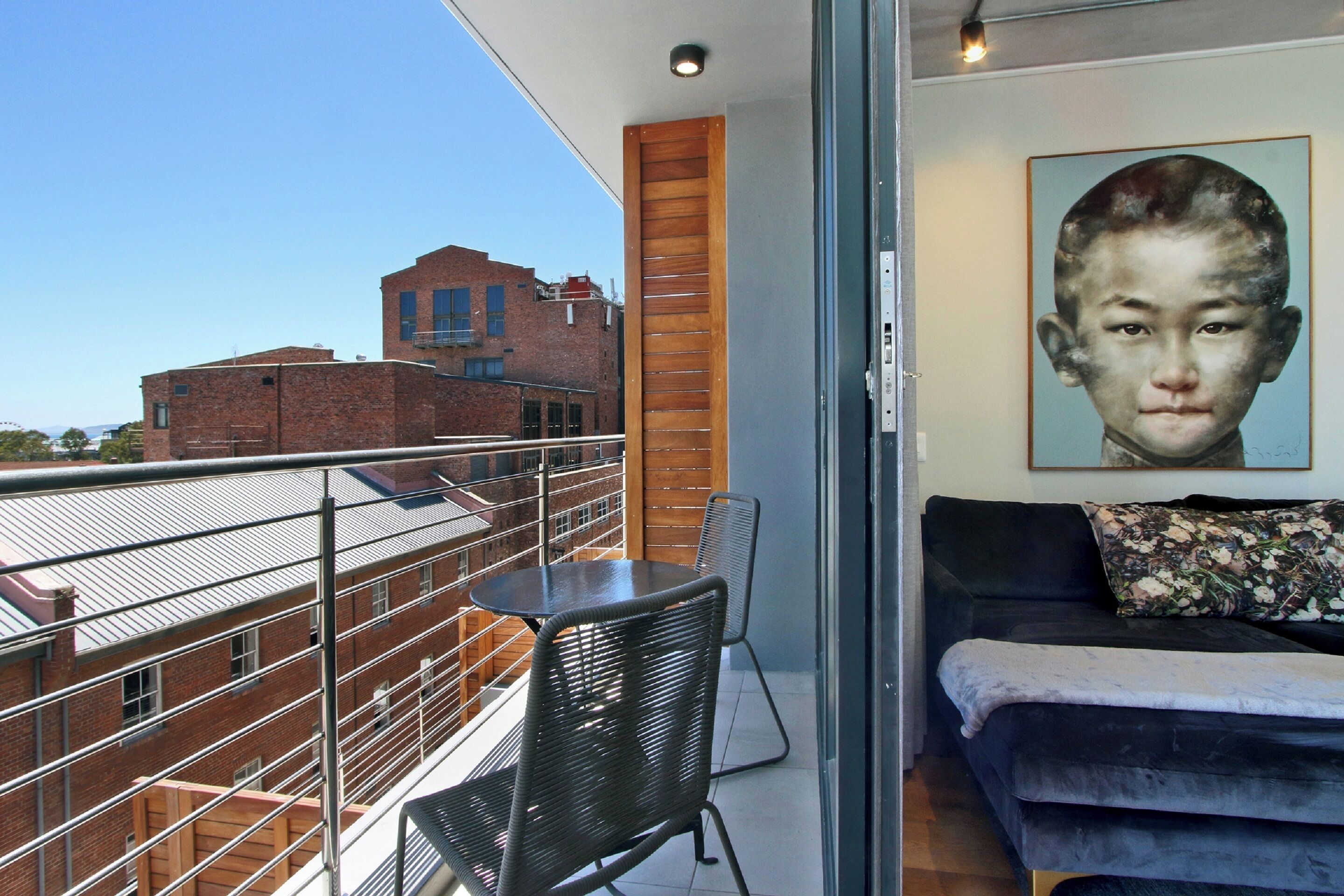 A balcony with a view of a brick building, a black metal chair, and a black sofa with a floral pillow.