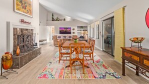 Uma sala de jantar ampla com mesa e cadeiras de madeira, um tapete colorido e uma lareira decorada.