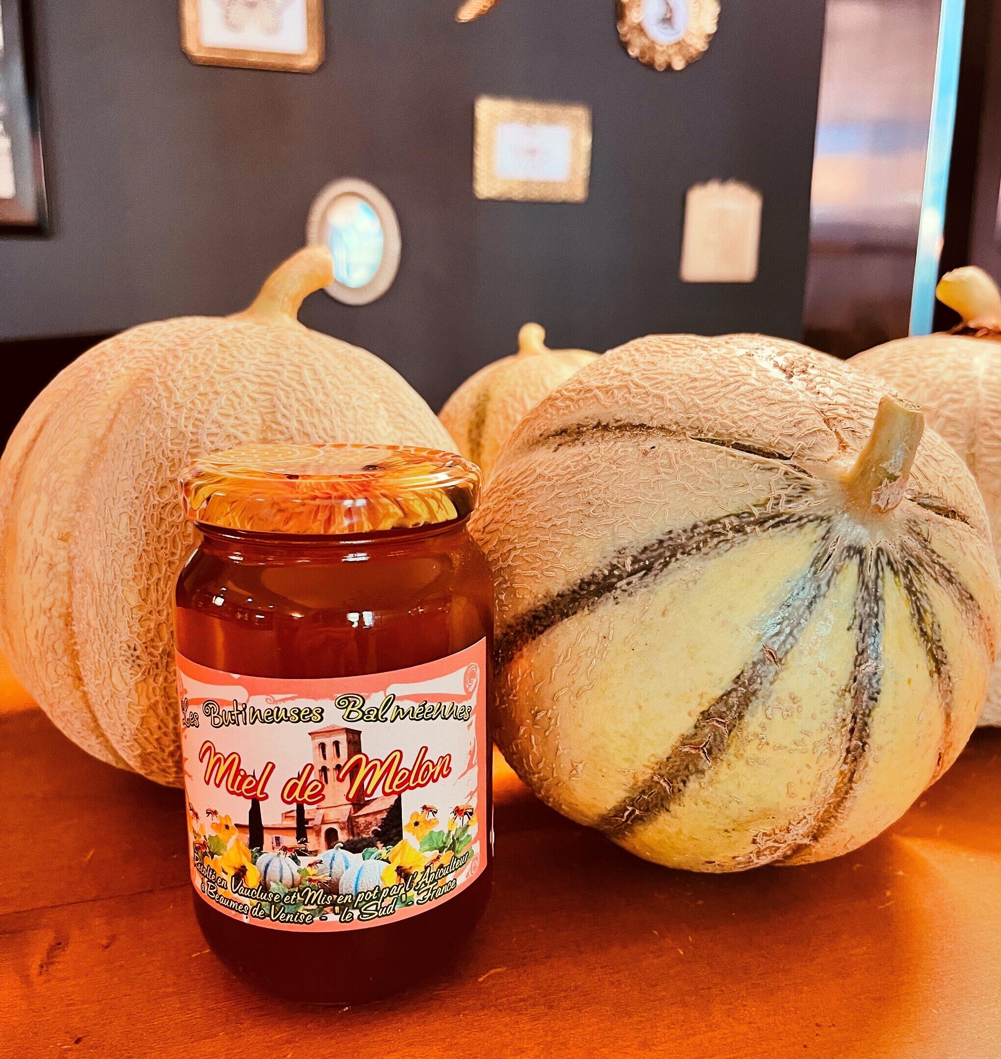 A jar of Miel de Melon with a label featuring a vintage illustration, placed on a table next to a pumpkin.