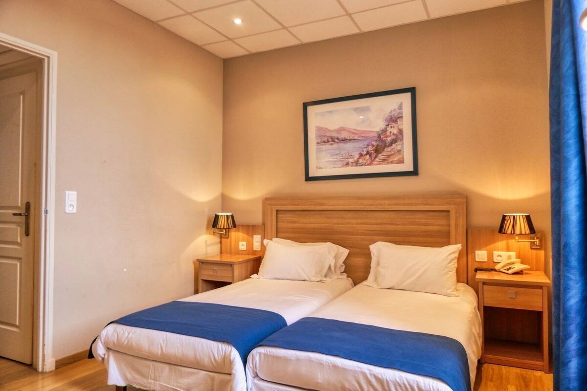 A double bed with two pillows, bedside tables with lamps, a framed picture on the wall, and a door.
