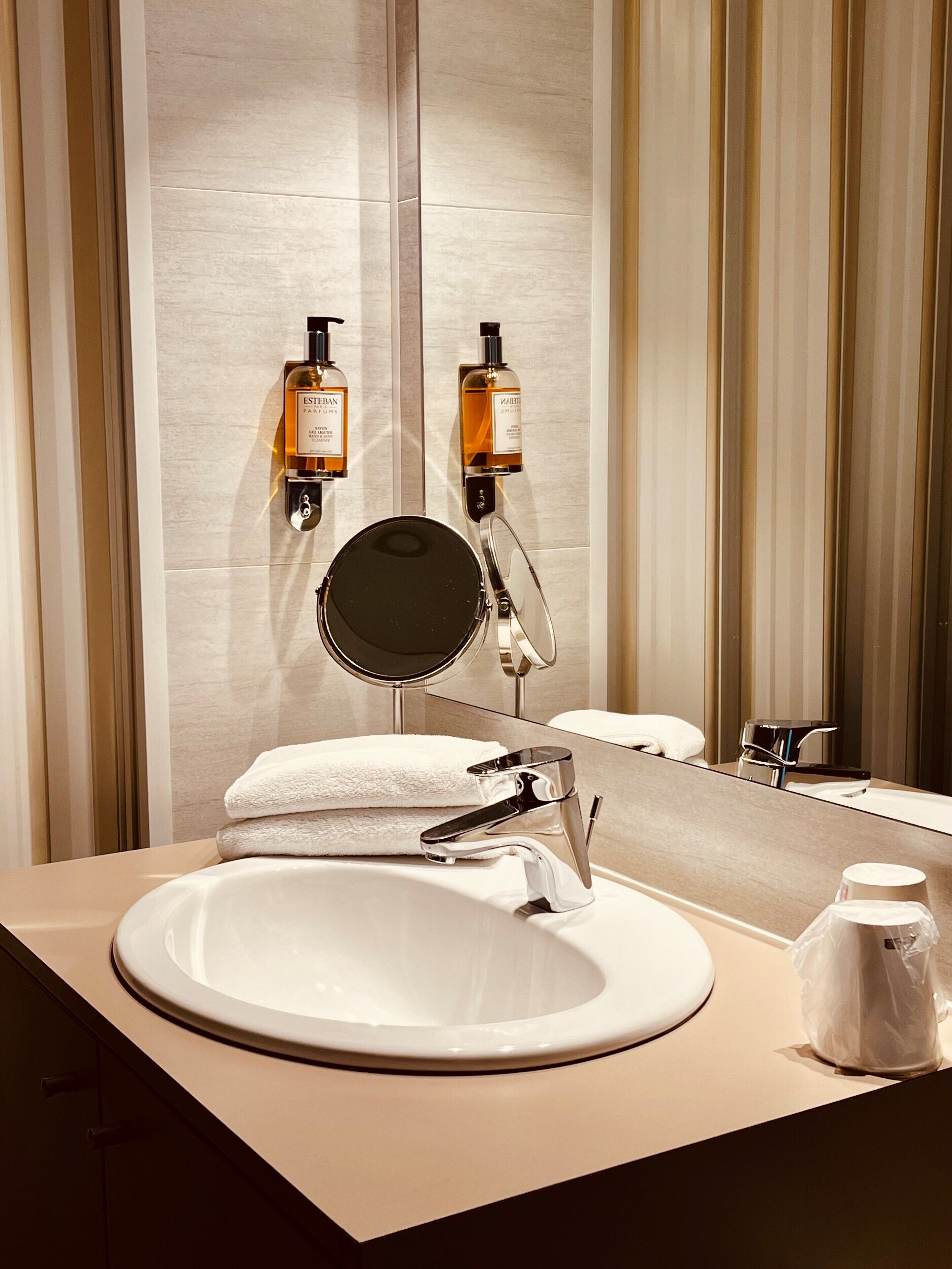 Een moderne badkamer met een ronde spiegel, een witte wastafel en twee toilettasflessen aan de muur.