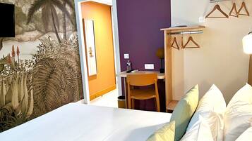Un dormitorio con cama, escritorio y silla. Una pared muestra un mural con paisaje tropical.