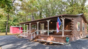 Eine Blockhütte mit Veranda, einer Flagge und einem roten Schuppen im Hintergrund.