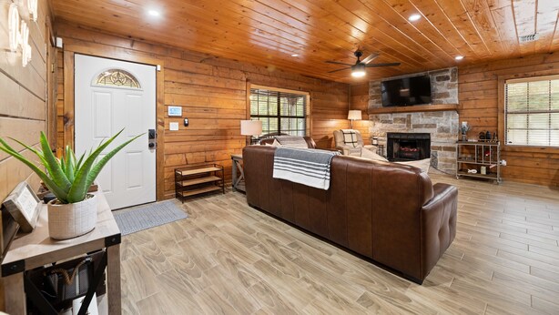 Ein rustikaler Blockhaushof mit Kamin, Ledersofa, Holzböden und einem über dem Kamin montierten Fernseher.