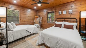 Eine Holzhütte mit zwei Betten, Deckenventilator und einem Fenster mit Jalousien.