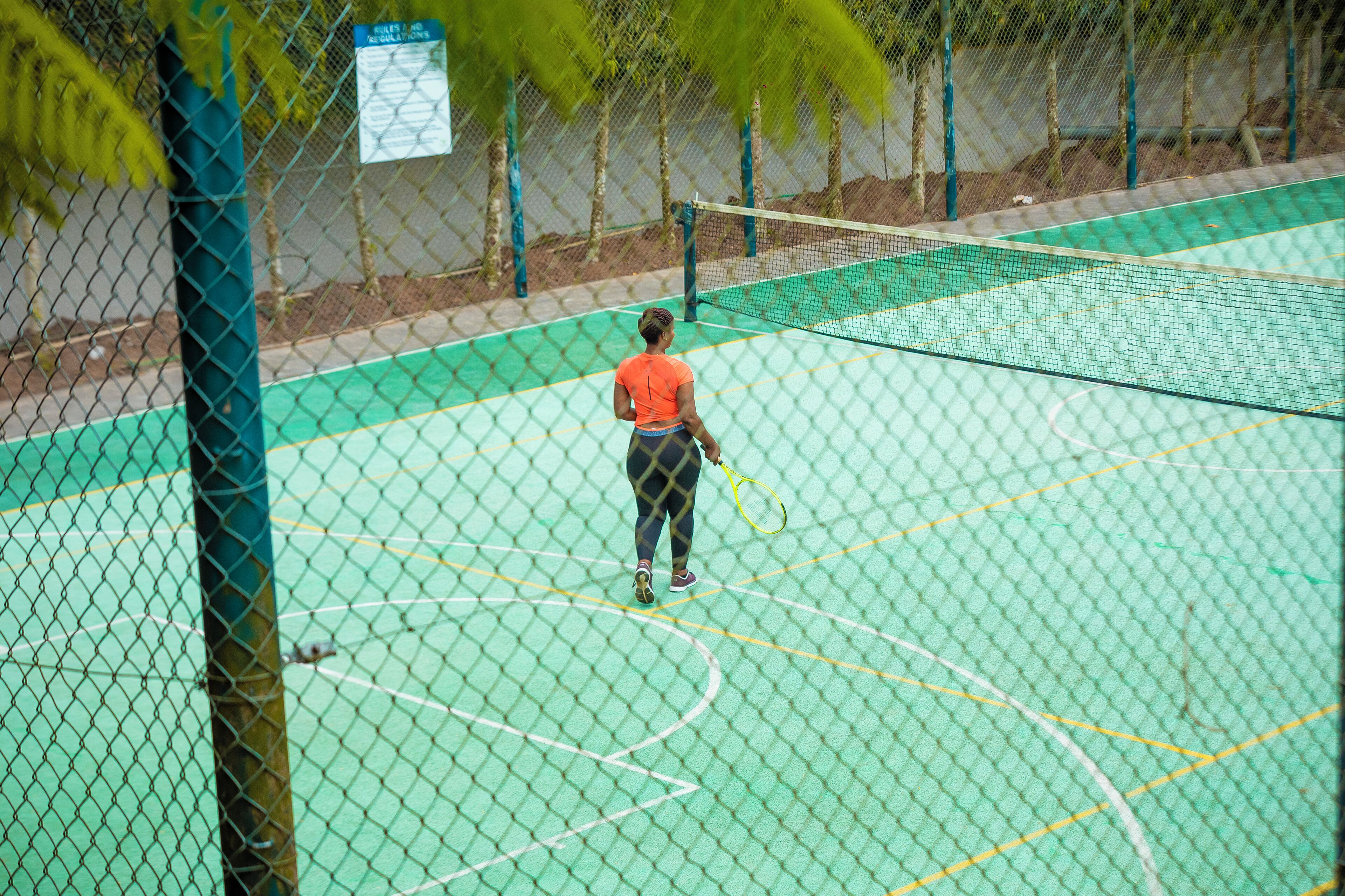 Una cancha de tenis con una red, rodeada por una cerca de malla metálica.